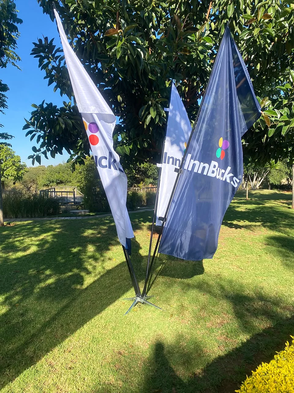 InnBucks branded feather flags on a cross base standing on a sunlit lawn